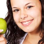 Junges Mädchen lächelt und hält Apfel in der Hand
