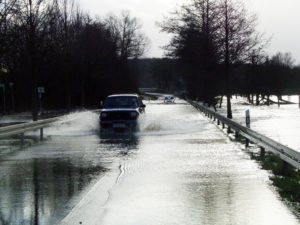 Überflutete Straße auf der ein Auto fährt