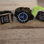 Drei Smartwatches liegen auf Holztisch nebeneinander