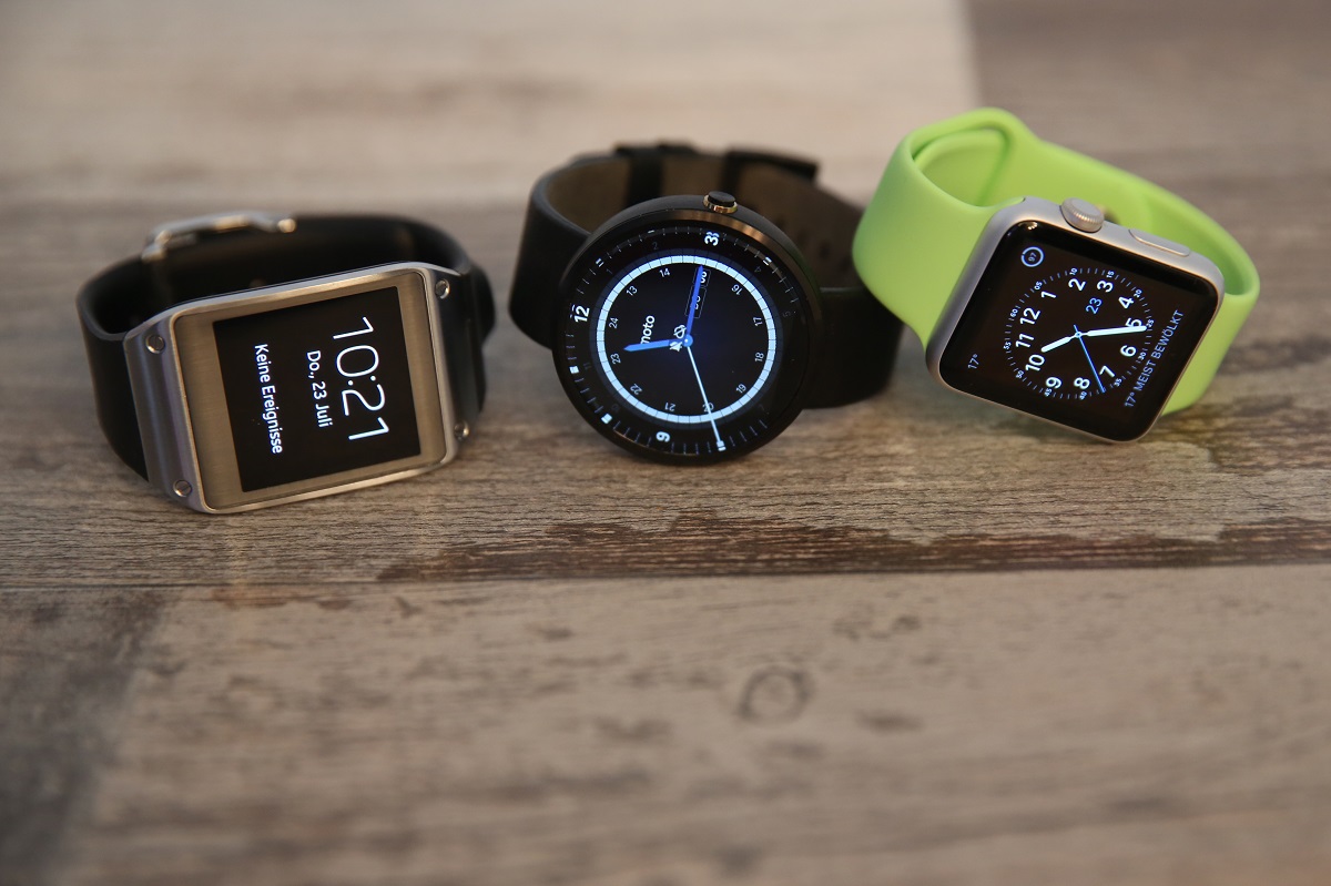 Drei Smartwatches liegen auf Holztisch nebeneinander